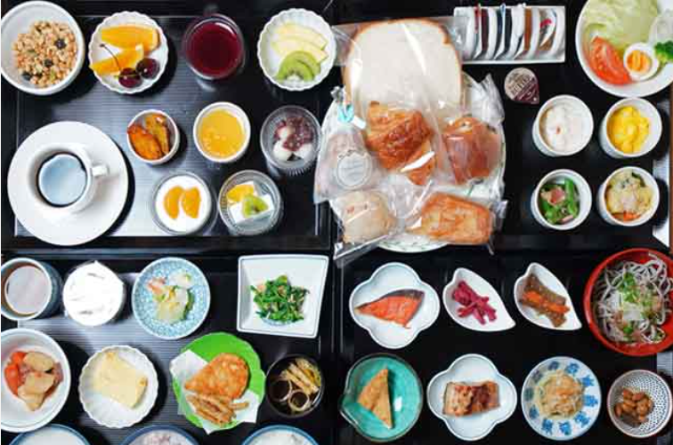 こちらは、豊富な朝食ビュッフェです。色とりどりの食材が並んだ朝食ビュッフェ。パン、フルーツ、サラダ、魚、卵料理などが小皿に盛られている。コーヒーとジュースも含まれており、バラエティ豊かな食事が楽しめる。