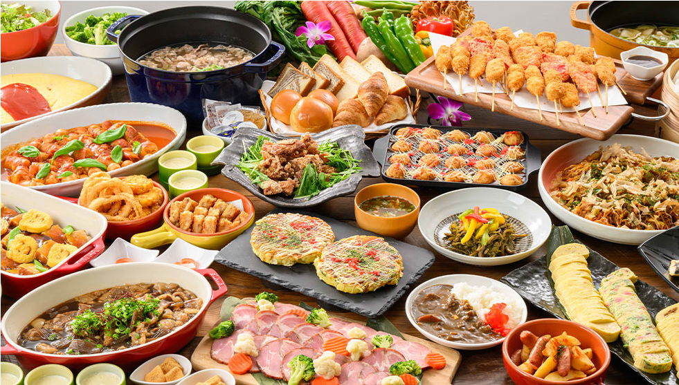 多彩な料理が並ぶビュッフェスタイルの食事です。串カツ、たこ焼き、炒め物、サラダ、カレーなど、バラエティ豊かなメニューがテーブルを彩っています。