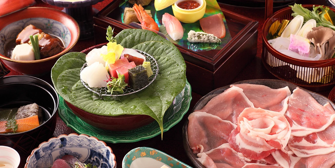 色とりどりの和食の料理がテーブルに並んでいます。刺身や煮物、しゃぶしゃぶ用の薄切り肉が美しく盛り付けられています。料理は季節の食材を使い、華やかな見た目をしています。