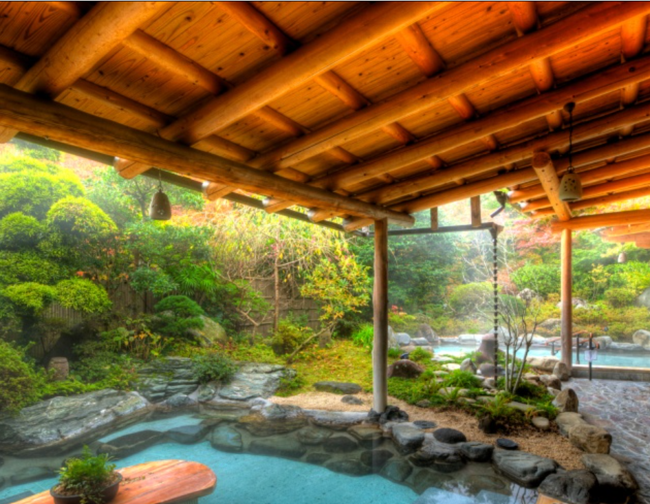 伝統的な日本の露天風呂です。木製の屋根の下に自然の石で囲まれた温泉があり、周囲には緑豊かな庭園が広がっています。