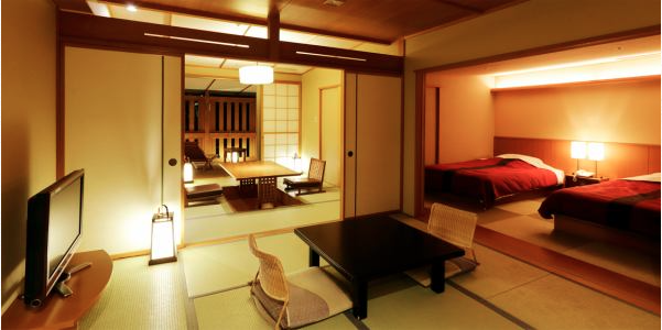 畳敷きの和室と洋室が一体となったホテルルーム。和室には低いテーブルと座椅子があり、奥の洋室には2つのベッドが配置されている。