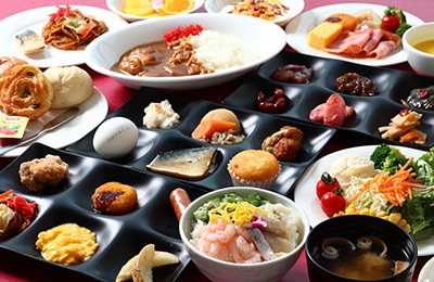  和洋折衷のビュッフェスタイルの朝食です。パン、カレー、サラダ、刺身、卵料理など多様な料理が並んでおり、色とりどりの食材が使用されています。