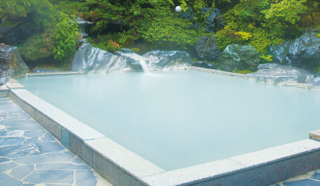 美しい自然に囲まれた露天風呂です。白濁した温泉が静かに湧き出ており、周囲には緑豊かな木々と岩が配置されています。