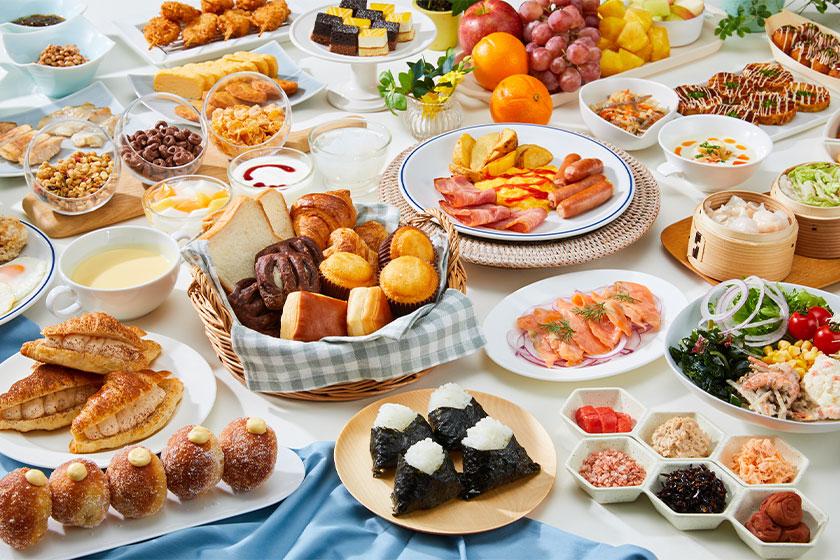 豊富な種類の朝食ビュッフェの写真です。テーブルには様々な料理が並べられており、パン、フルーツ、サラダ、焼き魚、卵料理、ソーセージ、おにぎりなどが見えます。色とりどりの料理が並び、食欲をそそる盛り付けがされています。