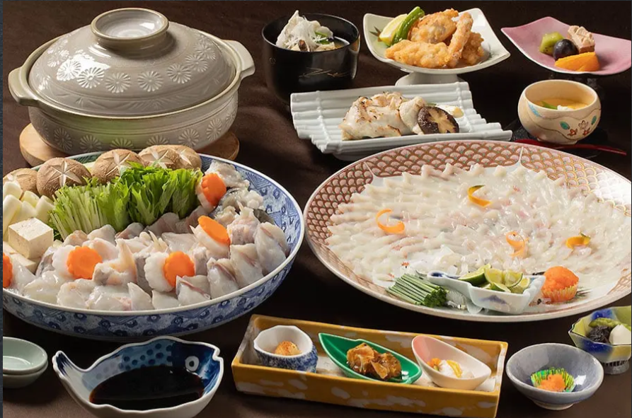 豪華な和食の宴会料理。大皿に盛られた刺身や鍋料理、揚げ物、茶碗蒸しなどが並んでいる。色とりどりの食器が使用されており、華やかで美しい盛り付け。