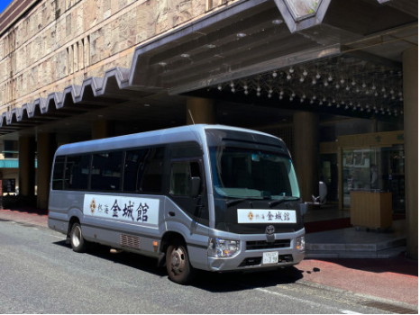 ホテルの玄関前に停車している小型バス。バスの側面には「金城館」と書かれており、建物の外観は豪華な装飾が施されている。バスは送迎用。