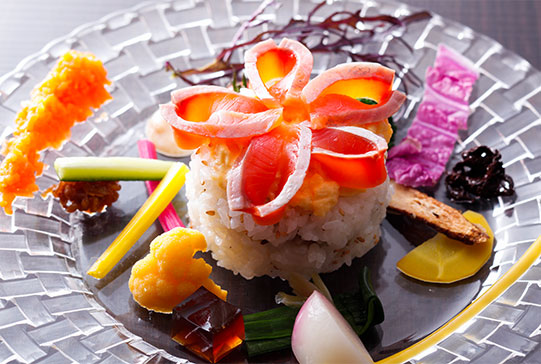 色とりどりの野菜がご飯の上や周囲に美しく盛り付けられたガラスのプレートの画像。