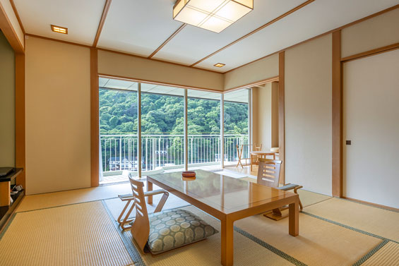 和室の画像。 畳敷きの部屋に低いテーブルと座布団が置かれている。大きな窓から緑豊かな山々の景色が見える。部屋の雰囲気は和モダンである。
